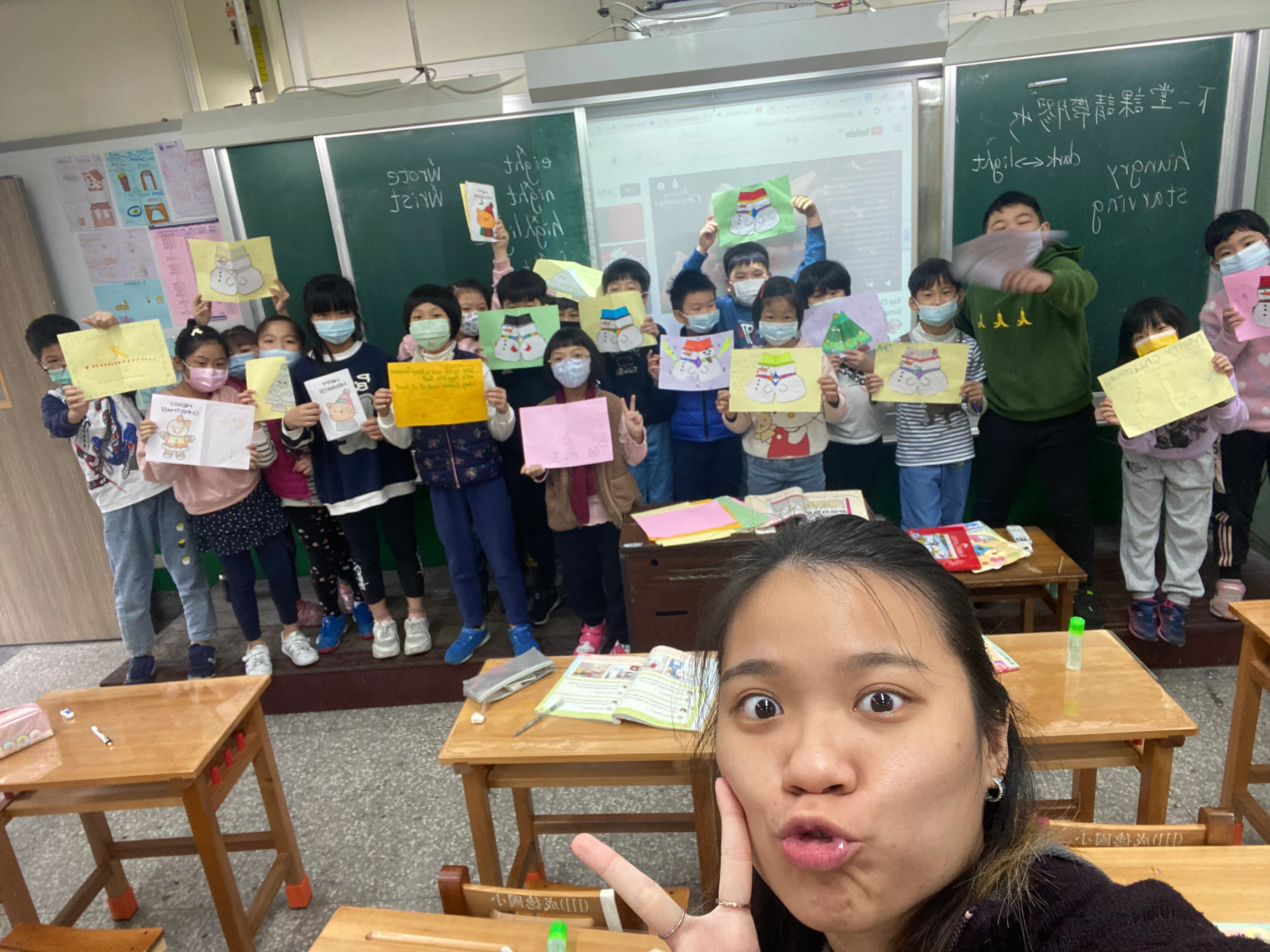 A classroom group holds up colorful student artwork for a photograph.