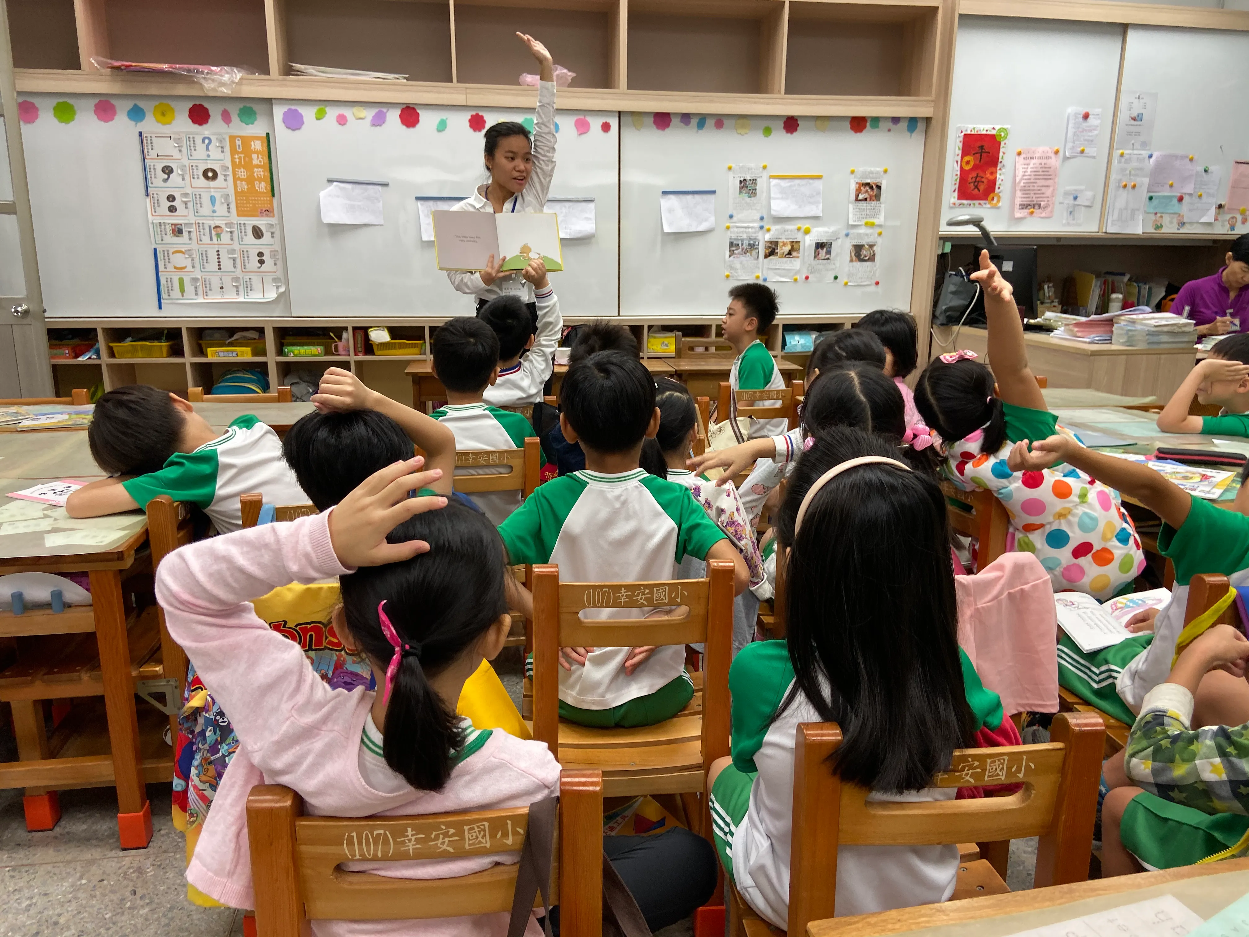 Yi Ling Pan reads to a classroom while students raise their hands.