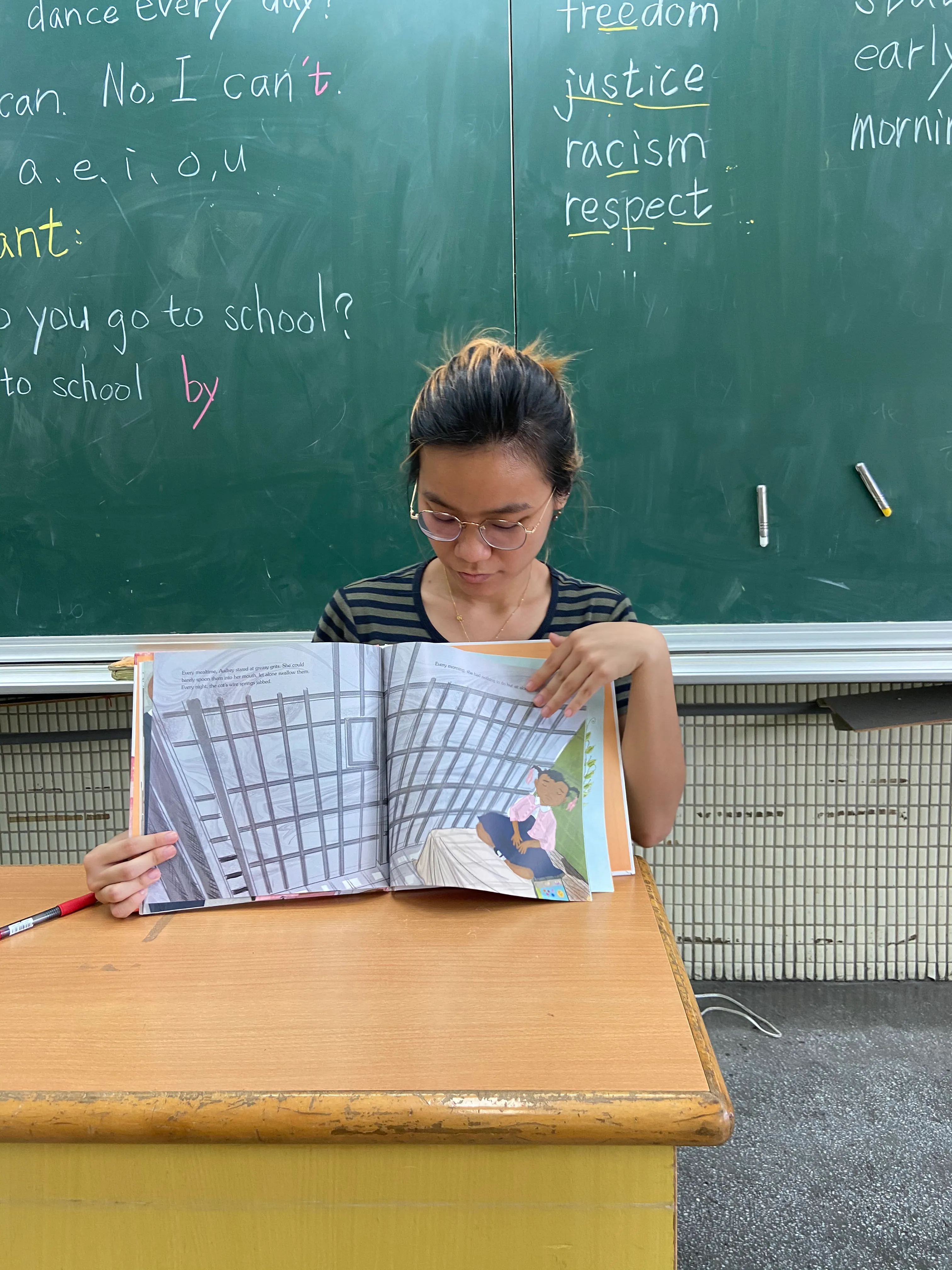 Yi Ling Pan reads an illustrated book in front of a chalkboard.