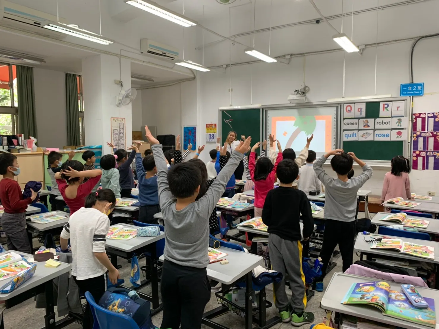 Yi Ling Pan leads a classroom activity while elementary students raise their arms.